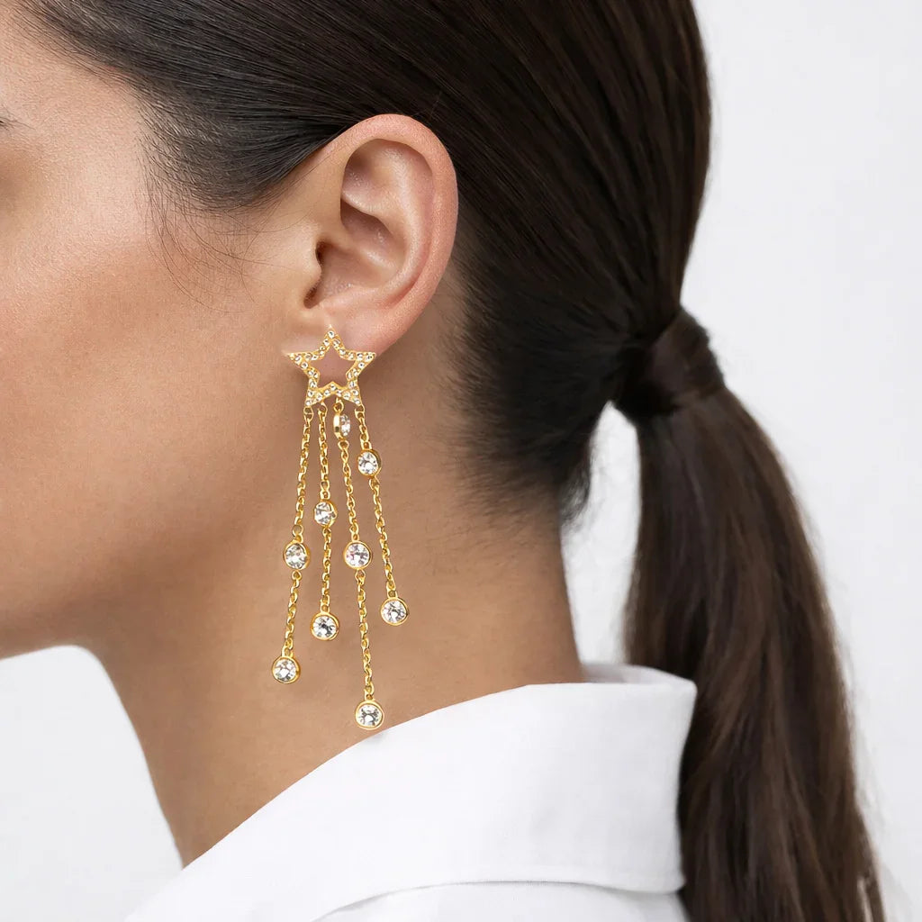 Gold star dangle earring with crystal accents worn by a woman with dark hair in a ponytail