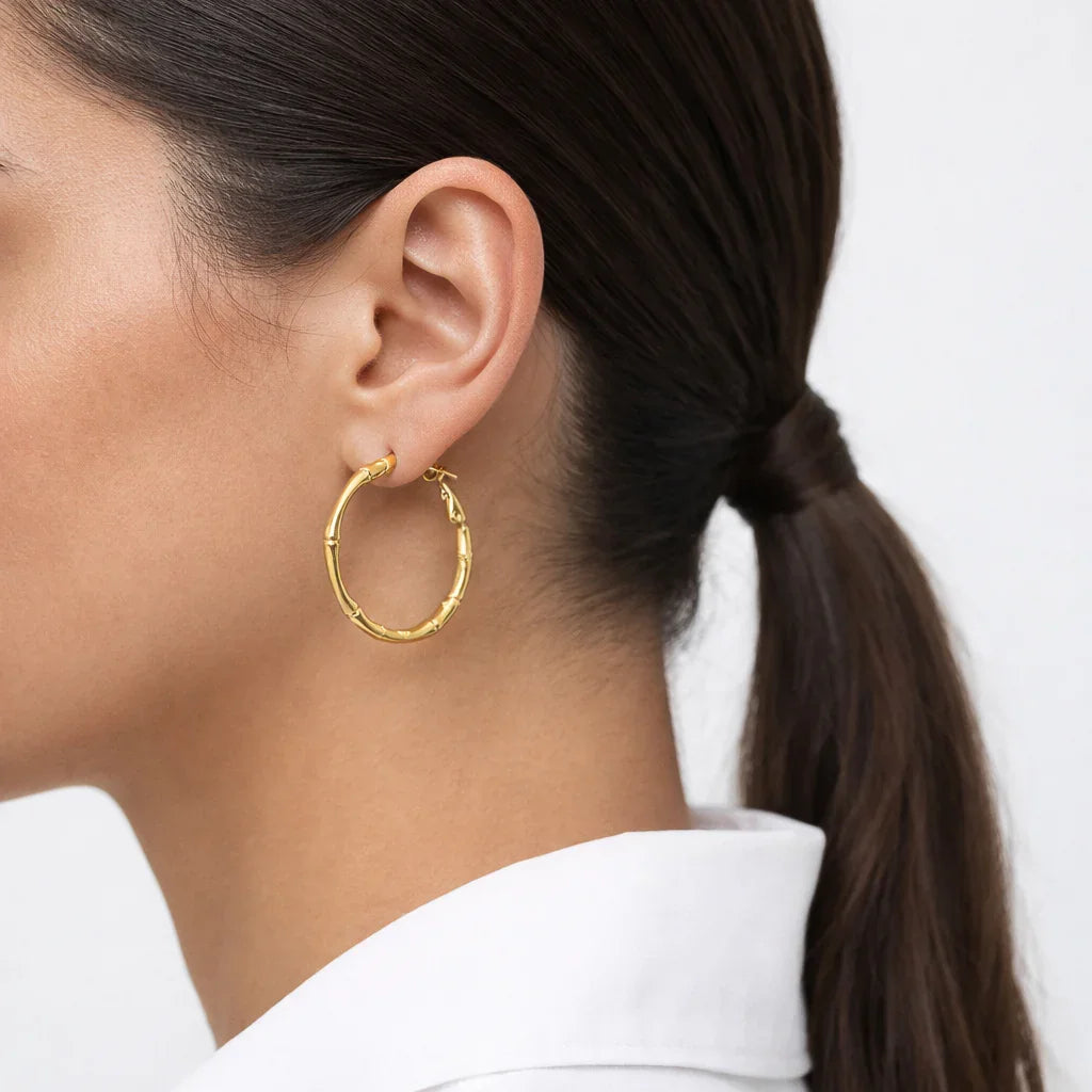 Gold bamboo hoop earring worn on woman with ponytail and white shirt