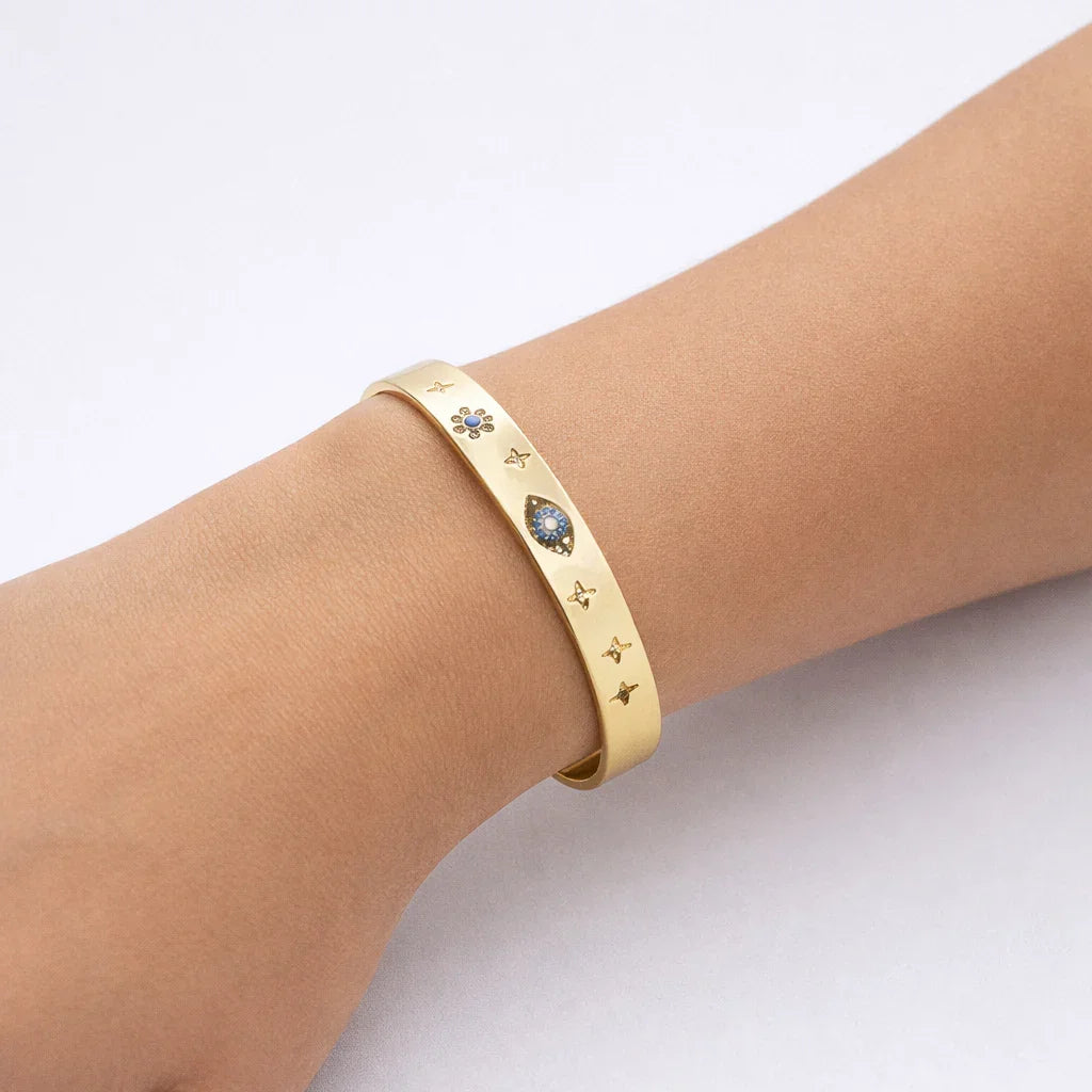 Gold cuff bracelet with engraved star and blue gemstone designs on wrist