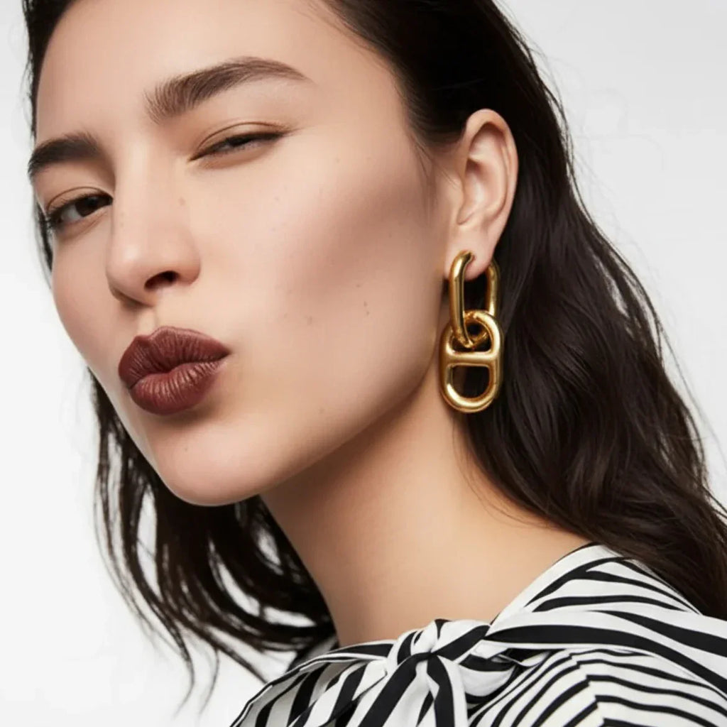Woman wearing chunky gold statement earrings and a black and white striped top